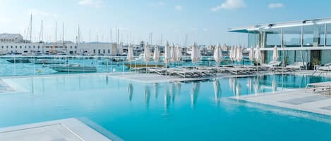 Un puerto deportivo con barcos y una piscina con sillas de descanso y sombrillas.