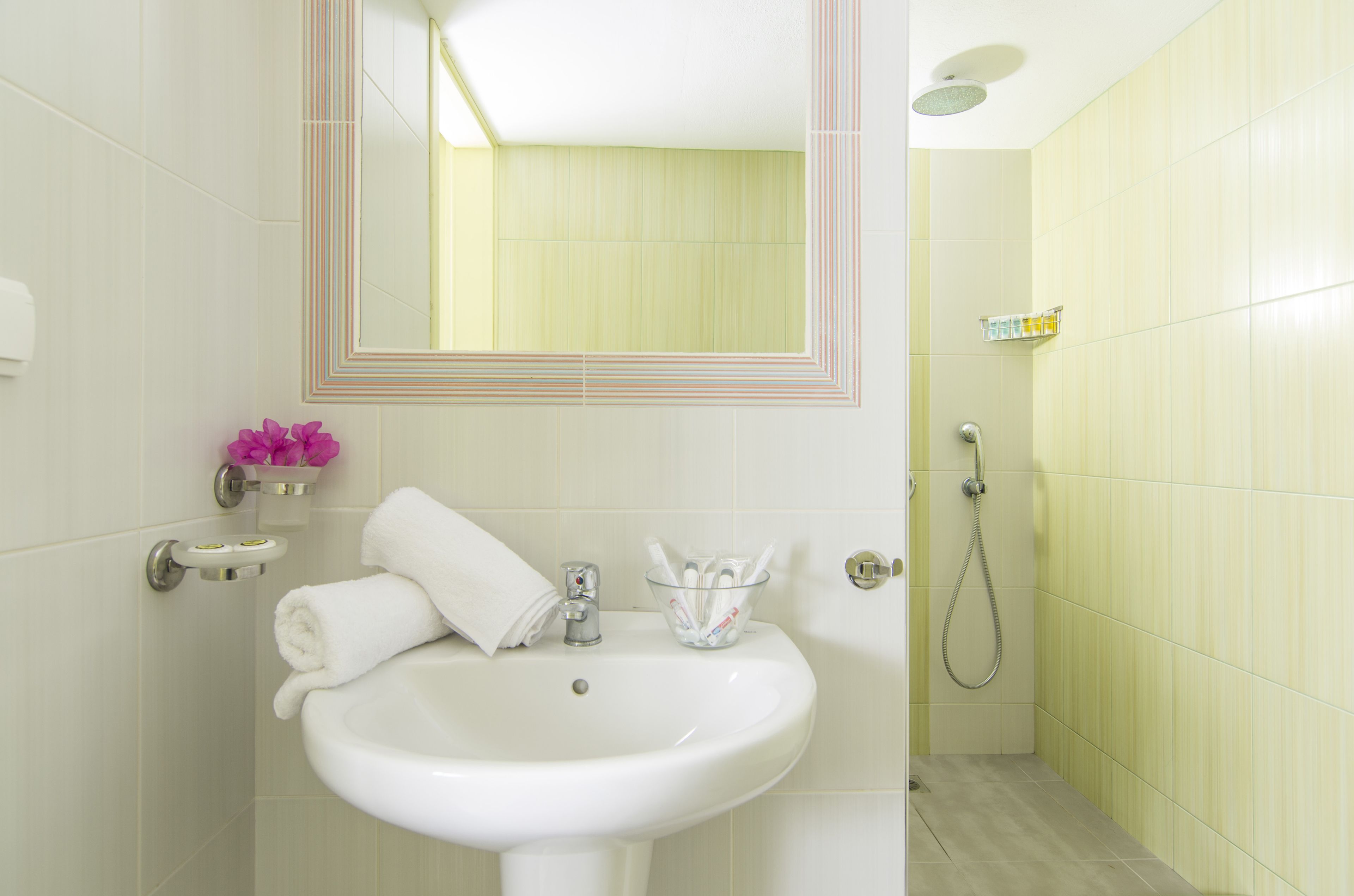 Ein Badezimmer mit einem weißen Waschbecken, einem Spiegel, einem Handtuch, einem Glasbehälter mit Zahnbürsten und einer Duschkabine.