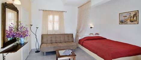A bedroom with a bed, a sofa, a small table, a mirror, and a painting on the wall.