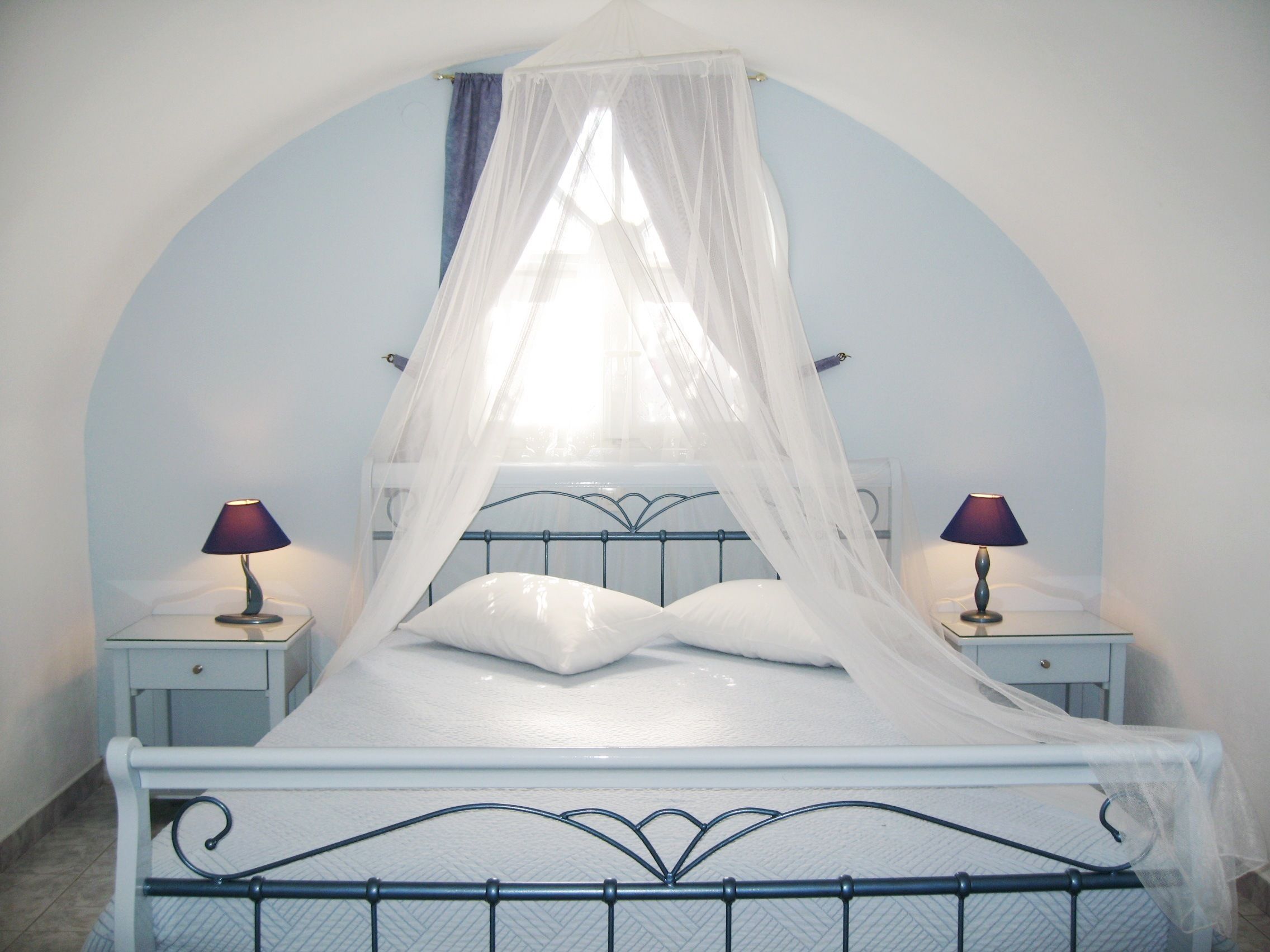 A bed with a canopy, two bedside lamps, and a nightstand with a lamp.