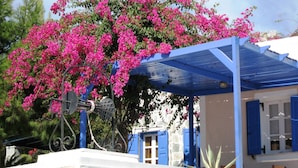 A building with a blue roof and white walls, surrounded by pink bougainvillea flowers. - Paradise Resort (Santorini)