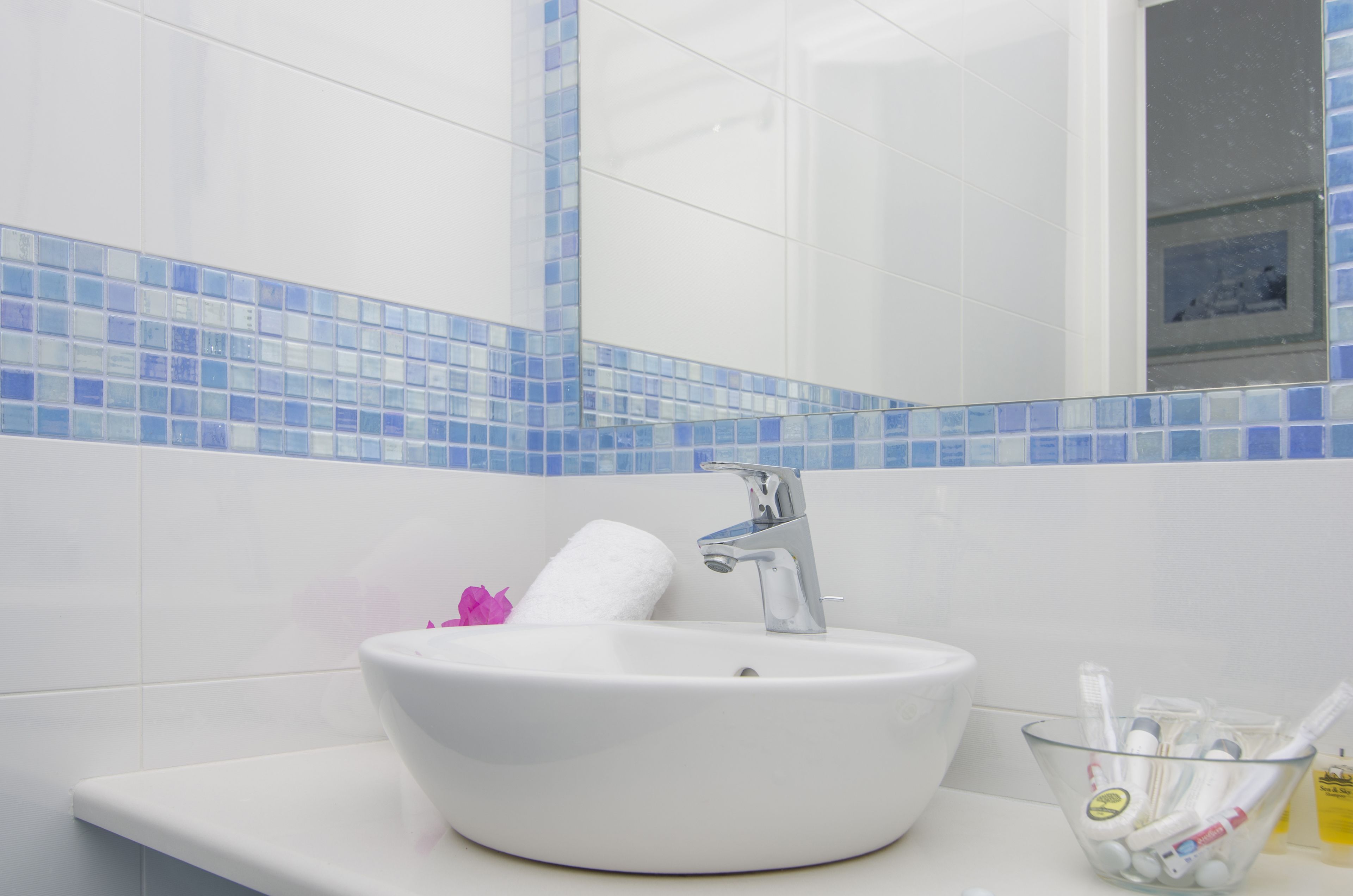 A bathroom with a white sink, a mirror, and a glass bowl containing toiletries.