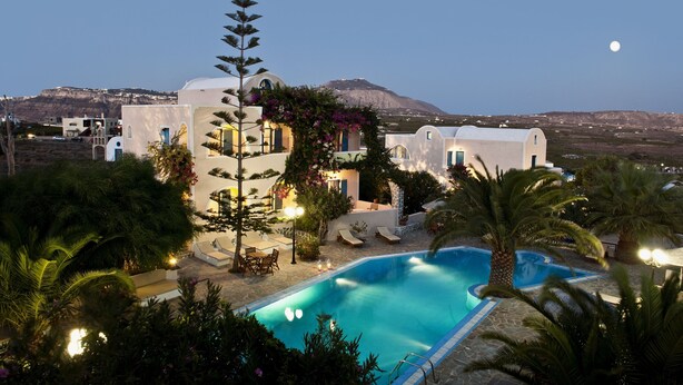 A resort with a swimming pool, palm trees, and a mountain in the background. - Paradise Resort (Santorini)