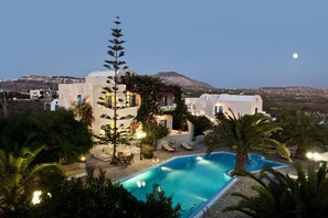 A resort with a swimming pool, palm trees, and a mountain in the background. - Paradise Resort (Santorini)