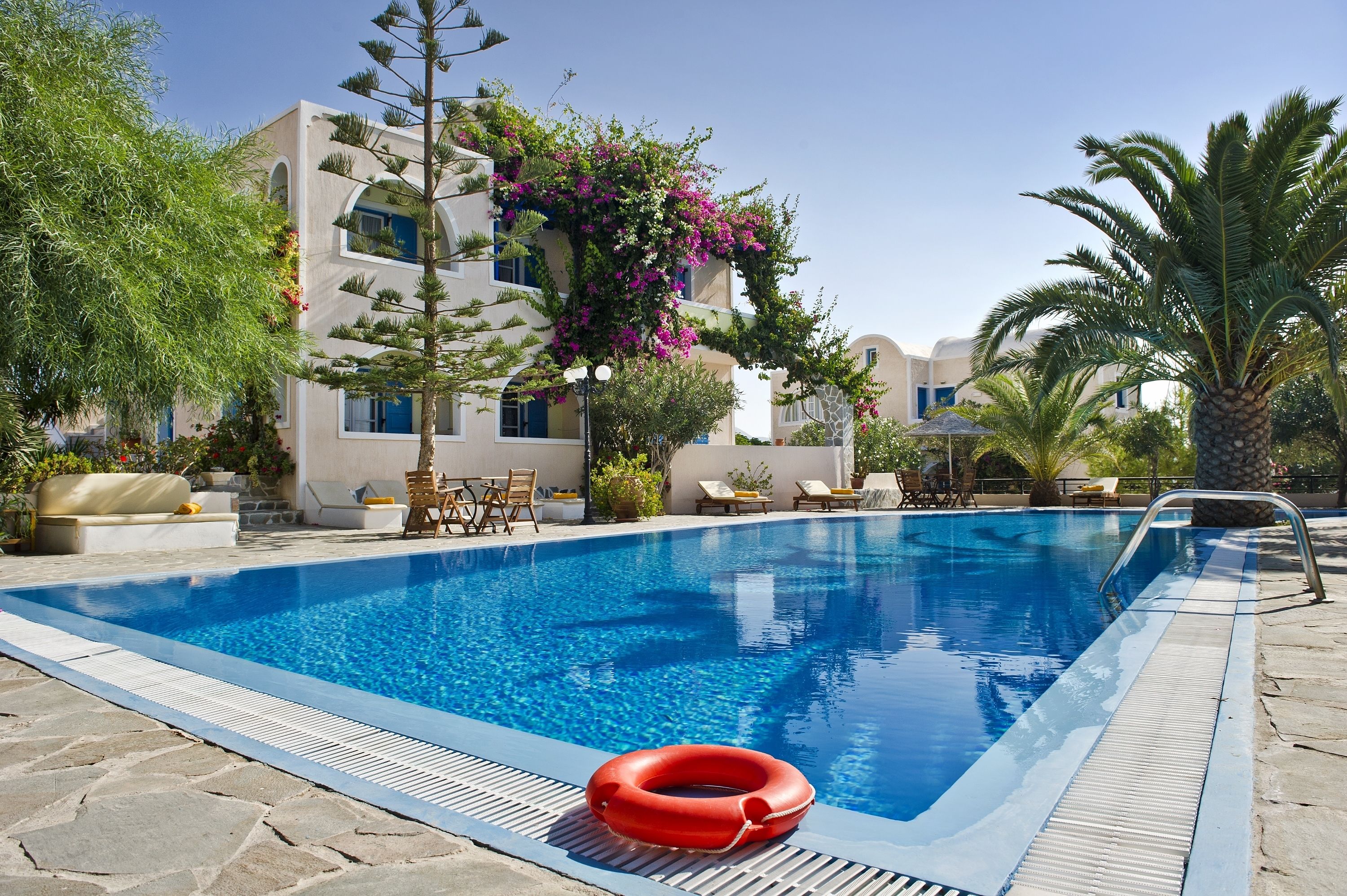 A swimming pool with a lifebuoy, surrounded by lounge chairs and a building with balconies.