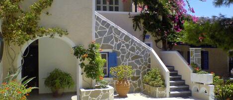 Un edificio con una escalera de piedra, un vestíbulo cubierto y plantas en macetas.