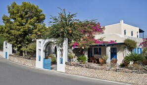 Un edificio de estilo mediterráneo con fachada blanca, contraventanas azules y un muro de piedra con guijarros.
