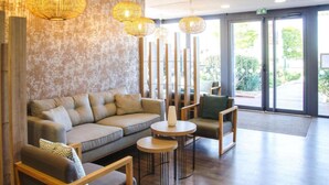 A modern lobby with a sofa, chairs, and round tables. - Le Provençal (Bordeaux)