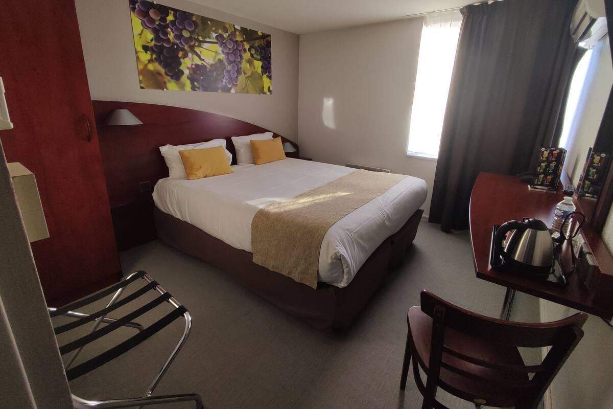 Une chambre d’hôtel avec un grand lit, un bureau, une chaise, une lampe et un tableau au mur.