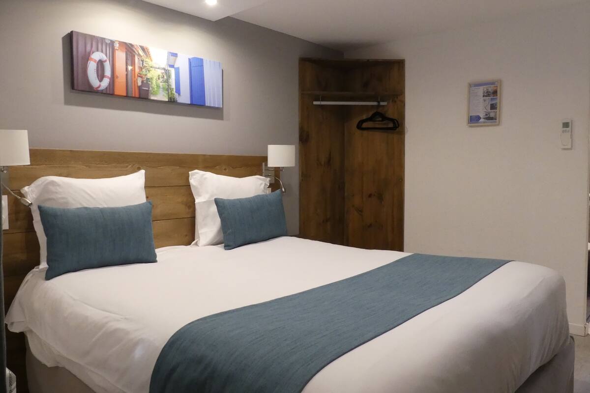 Un lit double avec une literie blanche et bleue, une tête de lit en bois et un plaid bleu.