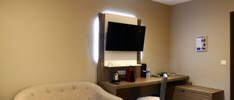 Habitación de hotel con sofá, escritorio con televisor de pantalla plana, una silla, cafetera pequeña y minibar.