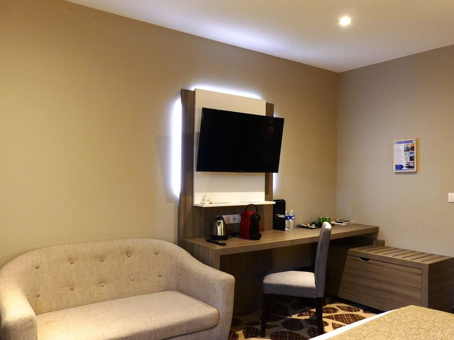Habitación de hotel con sofá, escritorio con televisor de pantalla plana, una silla, cafetera pequeña y minibar.