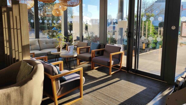 A modern interior with a sofa, chairs, and a small table. There are large windows with a view of the outside. - Le Provençal (Bordeaux)