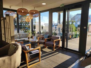 Un intérieur moderne avec un canapé, des fauteuils et une petite table. De grandes fenêtres offrent une vue sur l’extérieur.