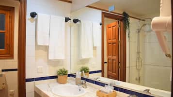 A bathroom with a large mirror, two sinks, a shower, and towels hanging on the wall.