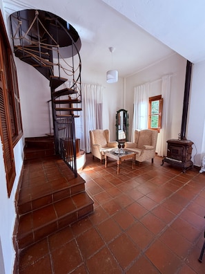 A spiral staircase leading to a second floor, a living room with two patterned armchairs, a coffee table, and a vintage stove. - Hotel Humaina (Málaga)