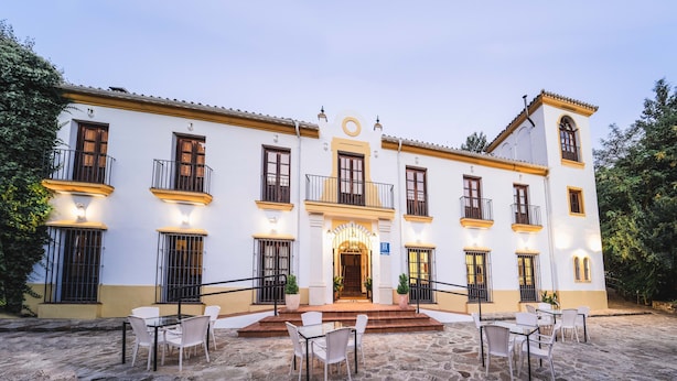 Un hotel con entrada central, varios balcones y zona de estar al aire libre.