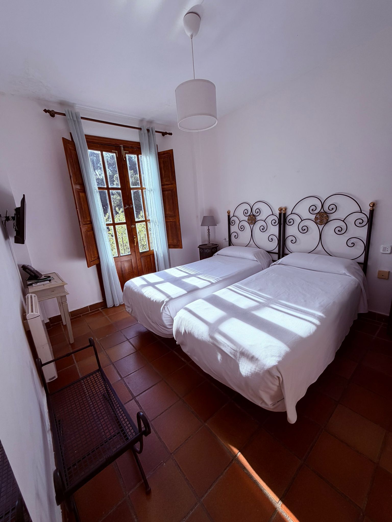 A bedroom with two beds, a desk, a chair, a lamp, and a window with curtains.