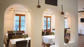 Un comedor con techos abovedados, mesas con manteles blancos y sillas de mimbre.