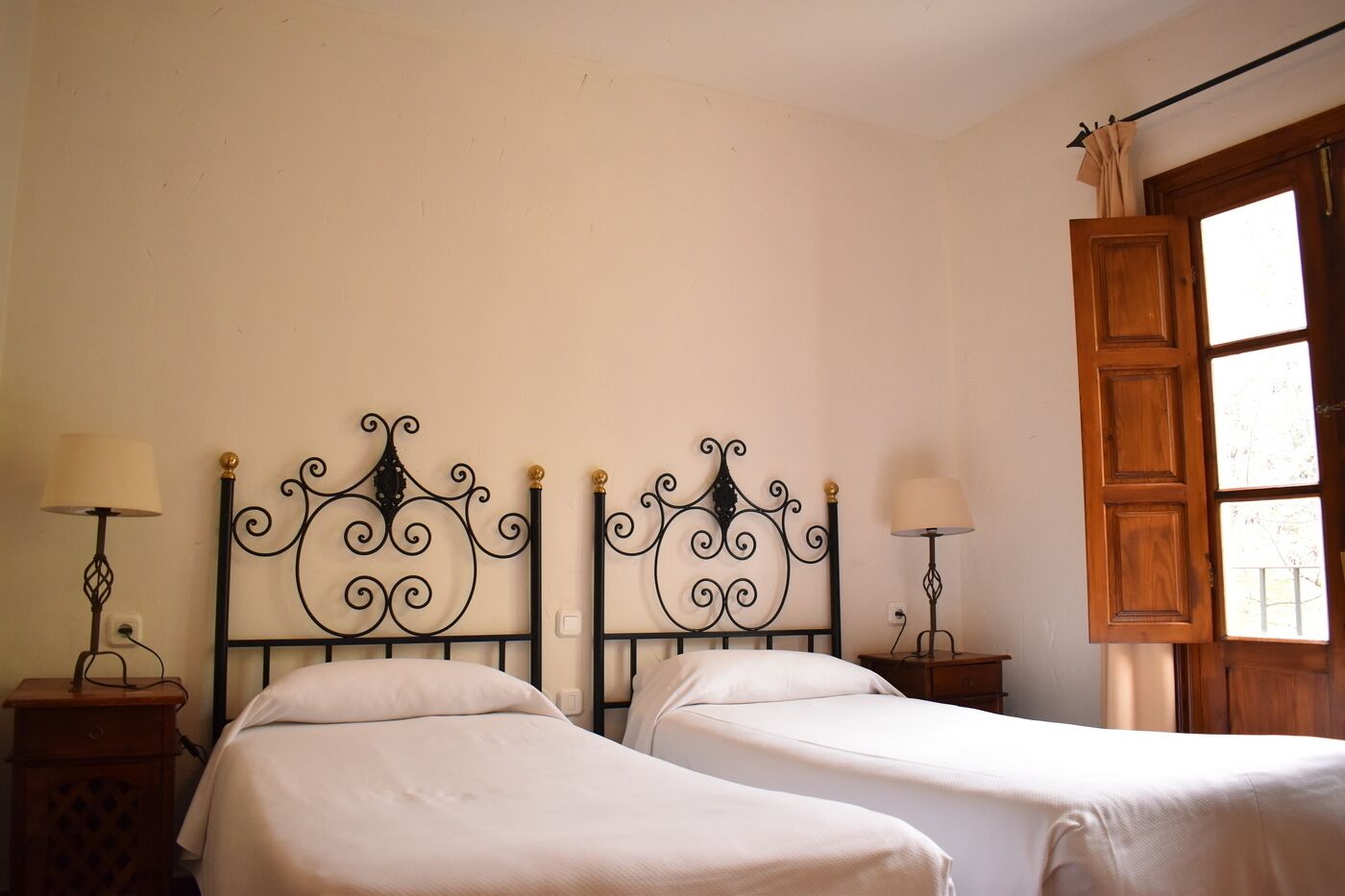 Una habitación con dos camas, cada una con un cabecero negro ornamentado y una mesita de noche con lámpara.