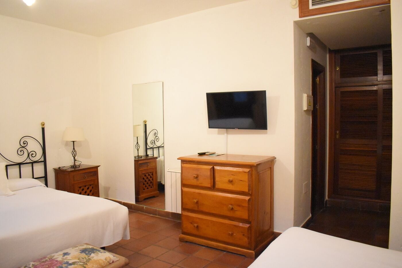 A bedroom with two beds, a wooden dresser, a television, and a mirror.