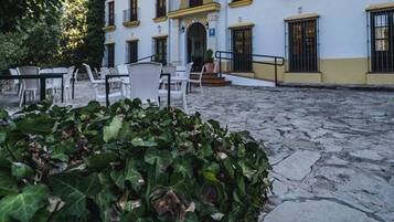 Un patio con edificios blancos, mobiliario exterior y suelo de piedra.