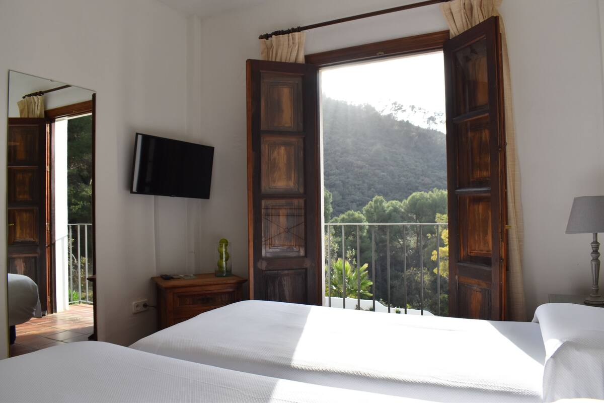 Ein Schlafzimmer mit Bett, einem an der Wand befestigten Fernseher und einem Balkon mit Bergblick.