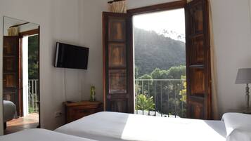 Een slaapkamer met een bed, een aan de muur bevestigde televisie en een balkon met uitzicht op de bergen.