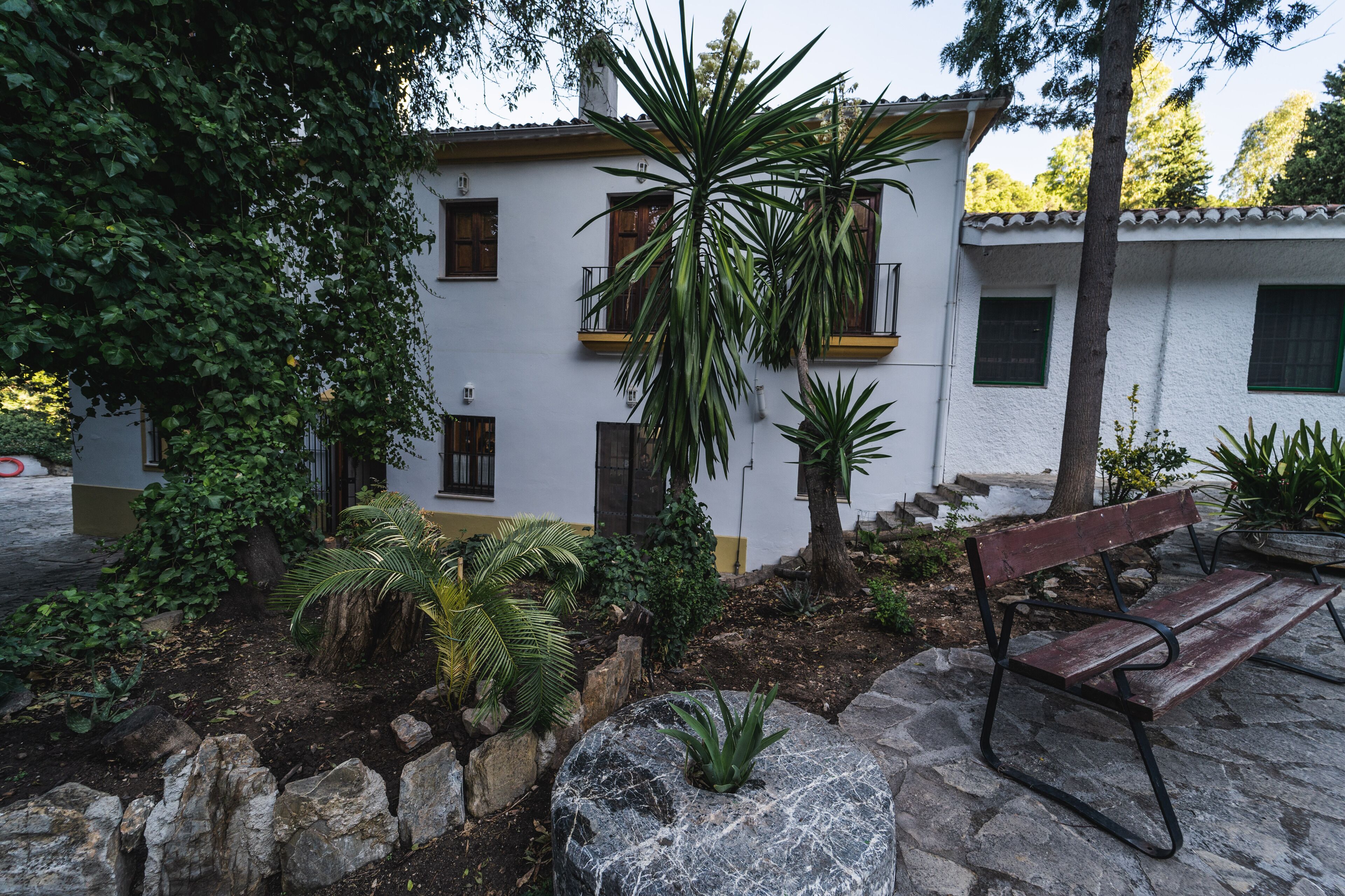 Un edificio con fachada blanca, varias ventanas y un banco de piedra en primer plano.