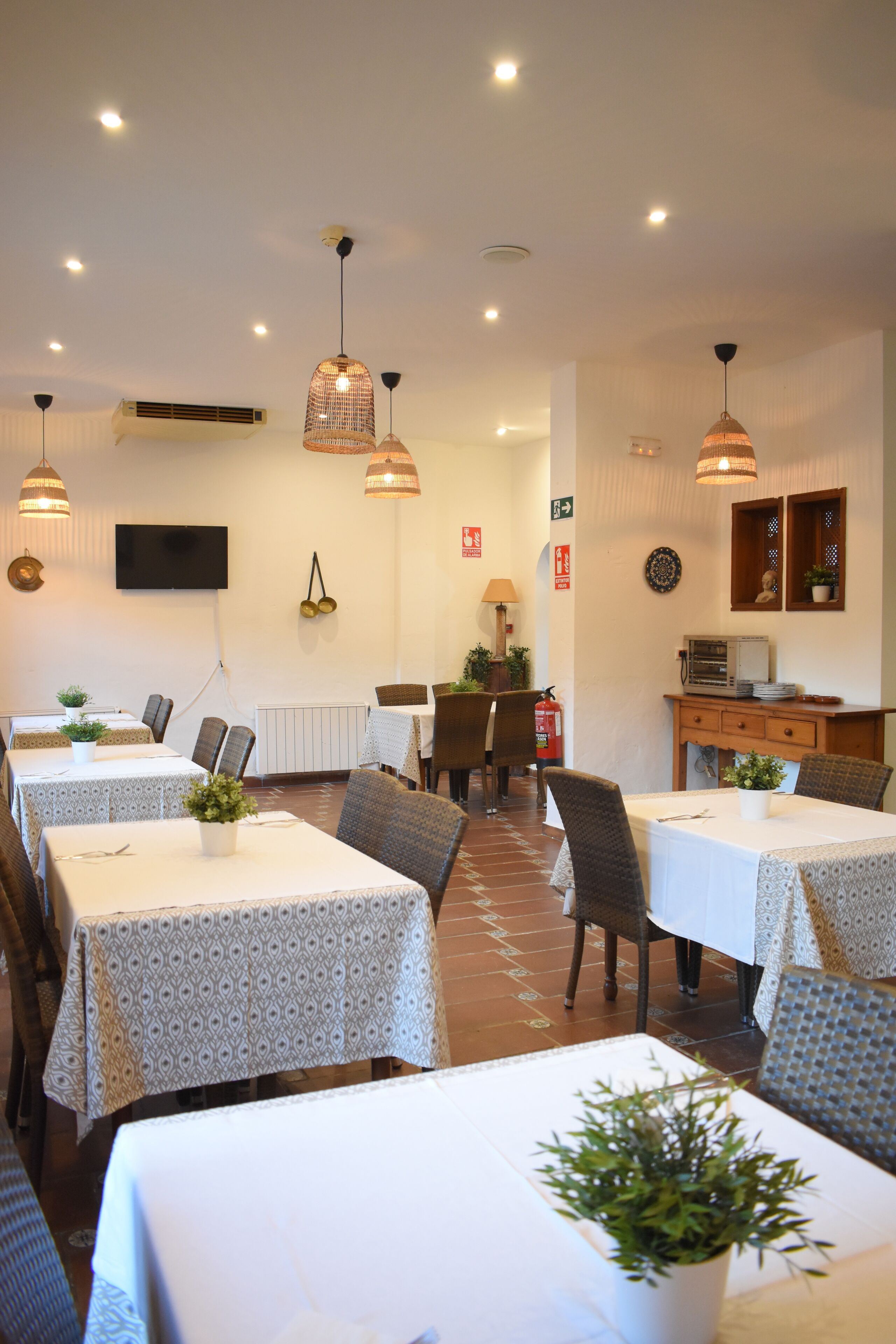 Comedor con mesas dispuestas para comer, iluminación en el techo y un televisor en la pared.