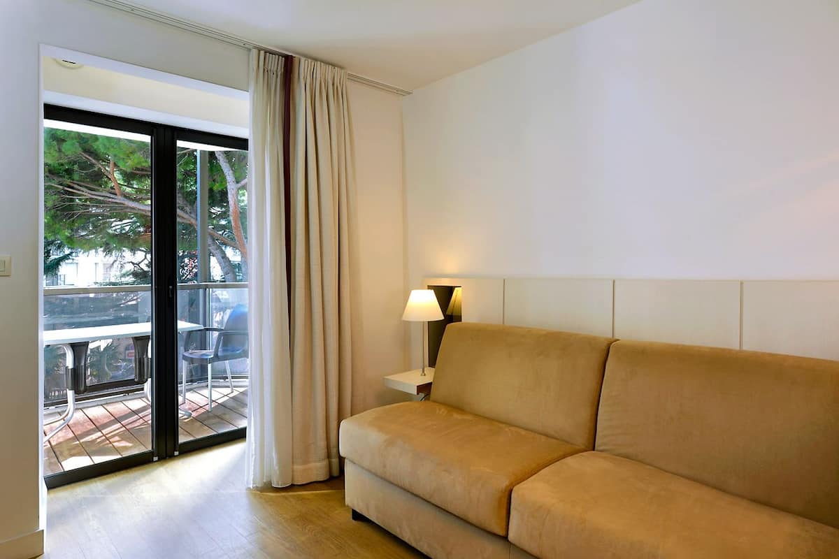 A hotel room with a sofa, a lamp, and a view of a balcony with chairs and a table.