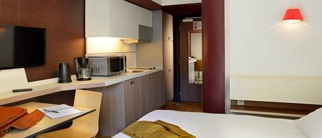 Habitación de hotel con cama, escritorio con silla, microondas, cafetera y televisión.