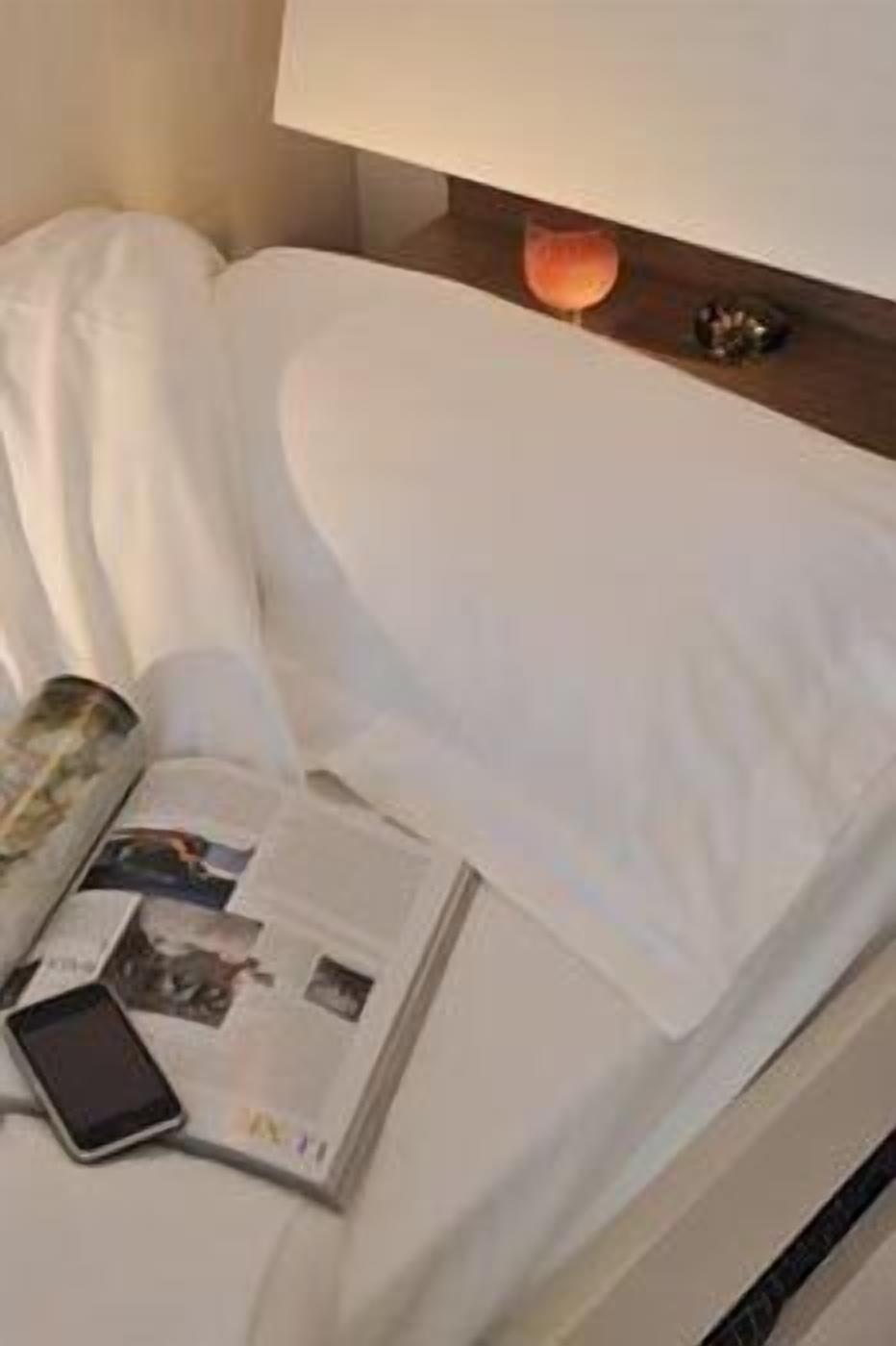 Una cama bien hecha con sábanas blancas, una revista y un teléfono inteligente sobre la cama.