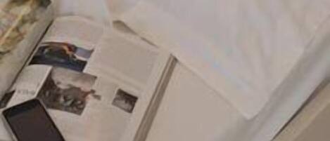 A neatly made bed with white linens, a magazine, and a smartphone on the bed.