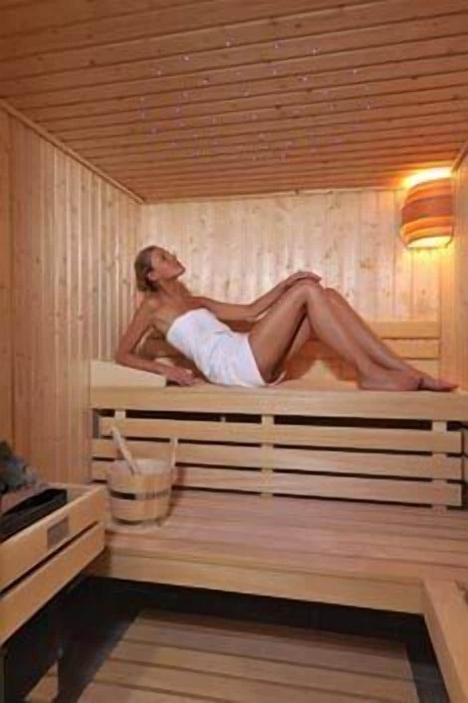 A sauna with wooden benches and a person lying on one.