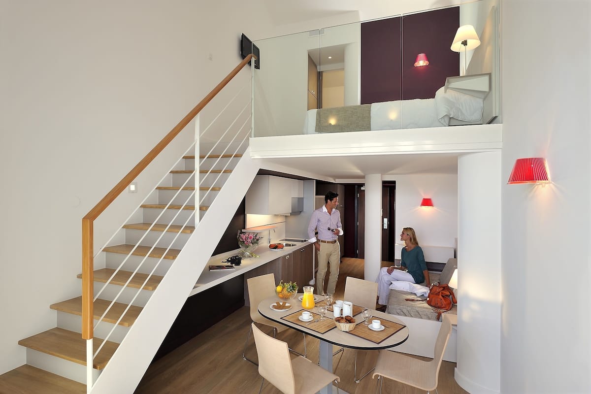A modern hotel room with a staircase, a dining area, and a bed.
