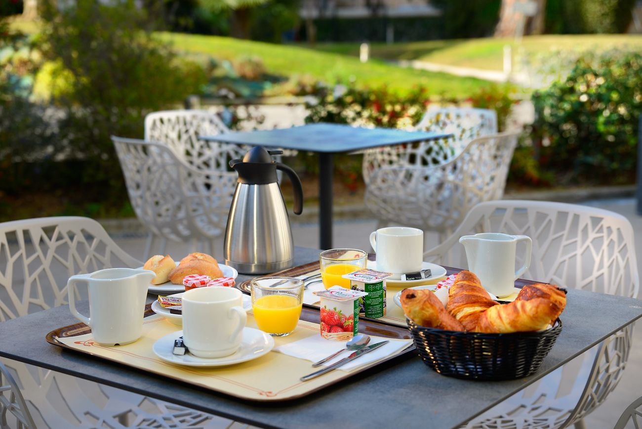 En frukostuppsättning med croissanter, juice och kaffe på ett utomhusbord med vita stolar.