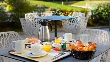 En frukostuppsättning med croissanter, juice och kaffe på ett utomhusbord med vita stolar.