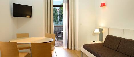 Una habitación de hotel moderna con comedor, sofá, televisor montado en la pared y vistas a través de una ventana.