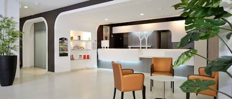 A modern lobby with a reception desk, seating area, and a large potted plant.