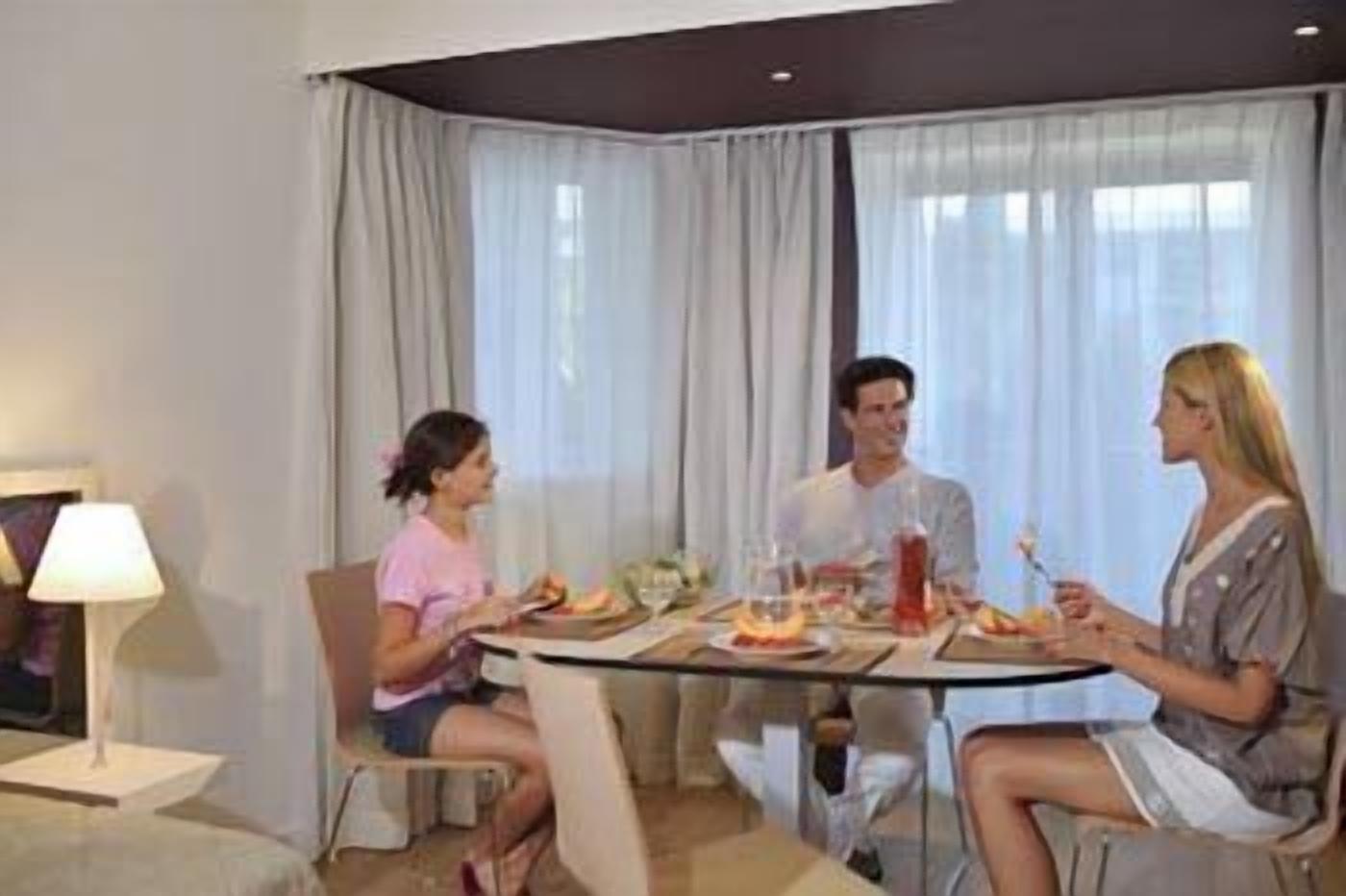 Un coin repas avec une table dressée pour quatre personnes, une lampe et une vue sur l’extérieur grâce à de grandes fenêtres.