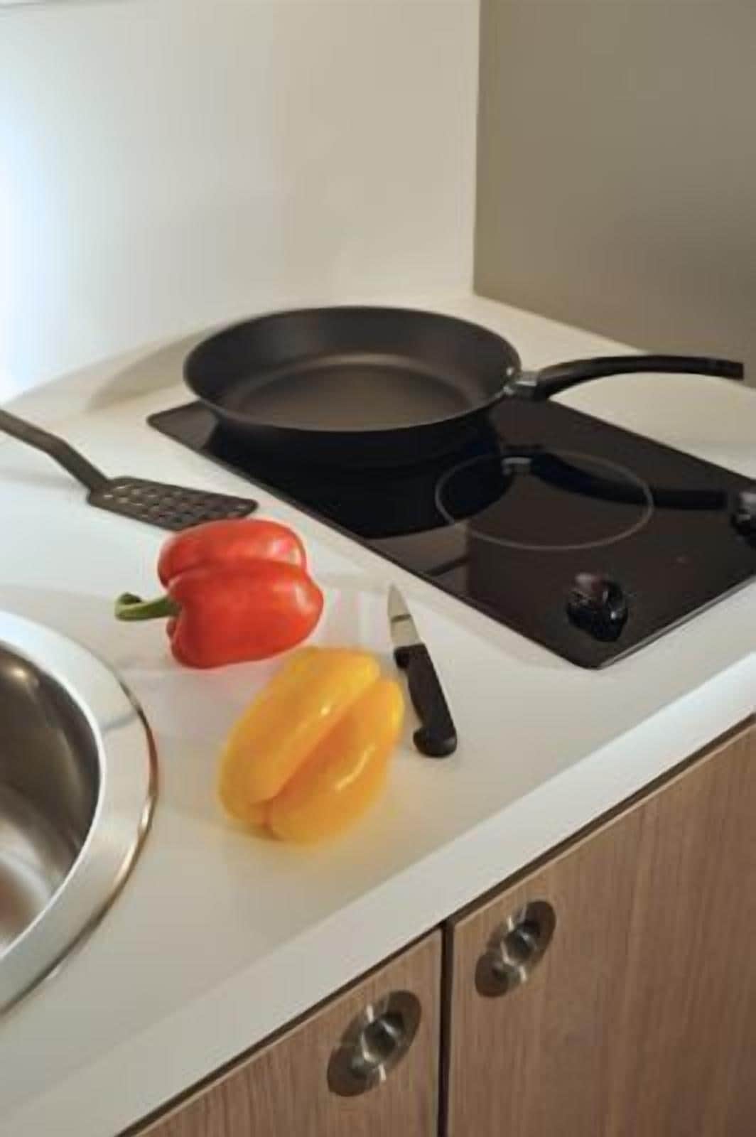 Une cuisine équipée d’une cuisinière, d’une poêle, d’un poivron rouge et d’un poivron jaune, ainsi que d’une râpe.