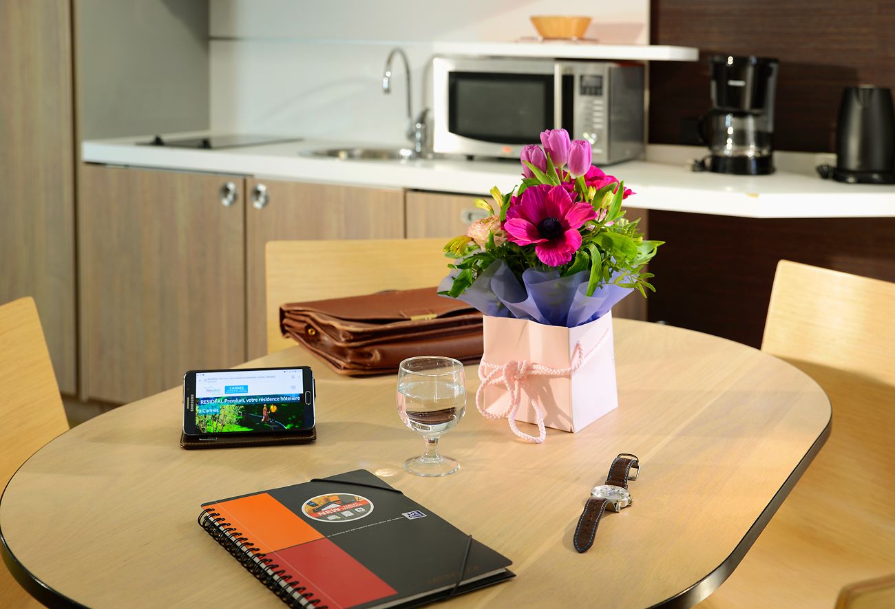 Un tavolo rotondo con un quaderno, uno smartphone, un bicchiere d'acqua, un orologio, un bouquet di fiori, una borsa regalo e una borsa in pelle marrone.