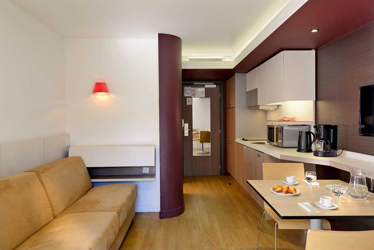 Ett modernt hotellrum med en soffa, ett matbord med tallrikar och glas, en kaffebryggare och en mikrovågsugn.