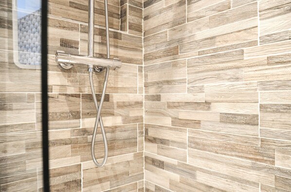 Un espace douche avec un mur carrelé et un pommeau de douche.