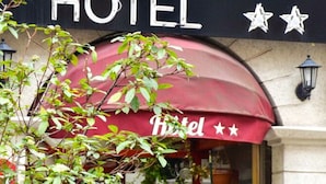 A hotel entrance with a red awning, potted plants, and a sign above the door. - Hôtel de la Perdrix Rouge (Paris)