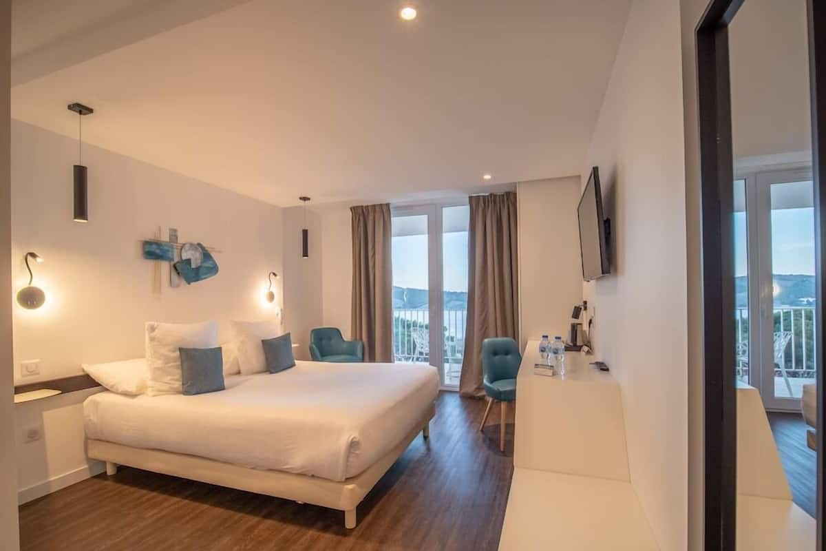 A hotel room with a bed, a desk, a chair, a TV, and a balcony with a view.