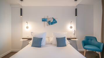A modern hotel room with a large bed, two bedside tables, a blue chair, and a wall-mounted artwork.