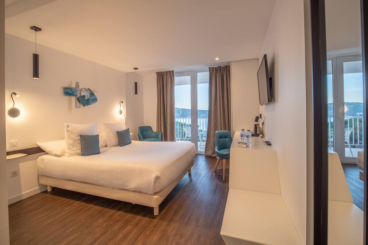 A modern hotel room with a large bed, a desk, and a view of the outdoors.