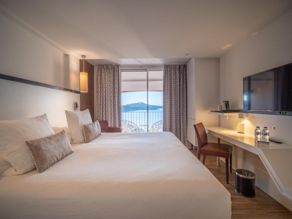 A hotel room with a large bed, a desk with a chair, a television, and a view of the outdoors.